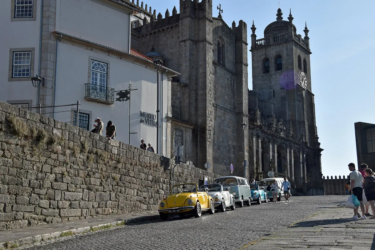 The granite towers of Porto Cathedral above a stone wall and a cobbled street.